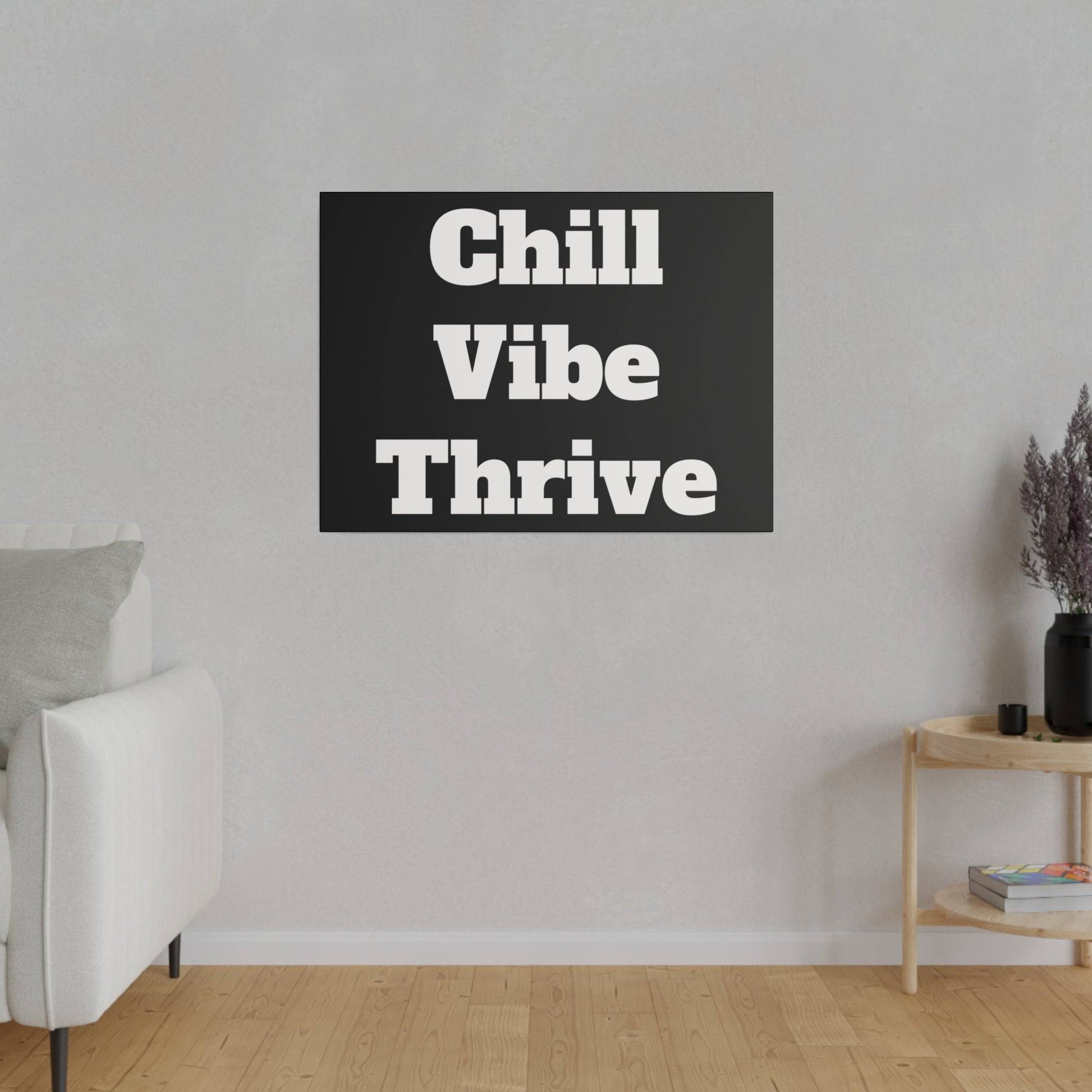 Black rectangular wall art with bold white text reading "Chill Vibe Thrive" hangs on a light gray wall above a white sofa.