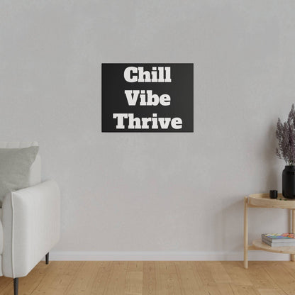 Black rectangular wall art with bold white text reading “Chill Vibe Thrive” hangs on a light gray wall above a wooden floor.