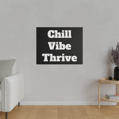 Black square wall art with bold white text "Chill Vibe Thrive" hung on a light gray living room wall above a wooden floor.