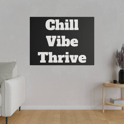 Living room scene with a black square wall art that says “Chill Vibe Thrive” above a white sofa.