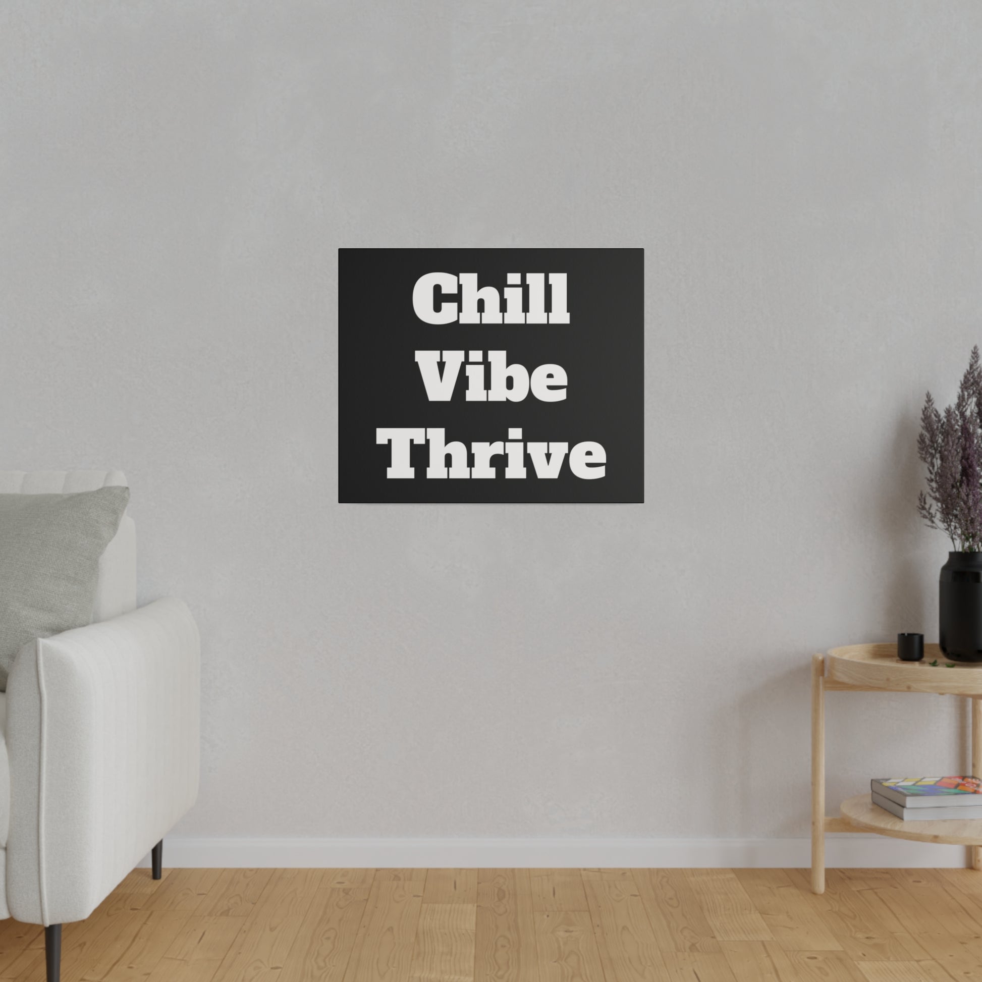Gray living room wall with a black square sign reading "Chill Vibe Thrive" centered above a white sofa; a wooden side table with a vase