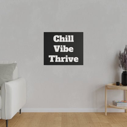 Gray living room wall with a black square sign reading "Chill Vibe Thrive" centered above a white sofa; a wooden side table with a vase