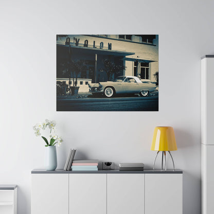 A vintage light-blue car parked on the street in front of a beige mid-century building.