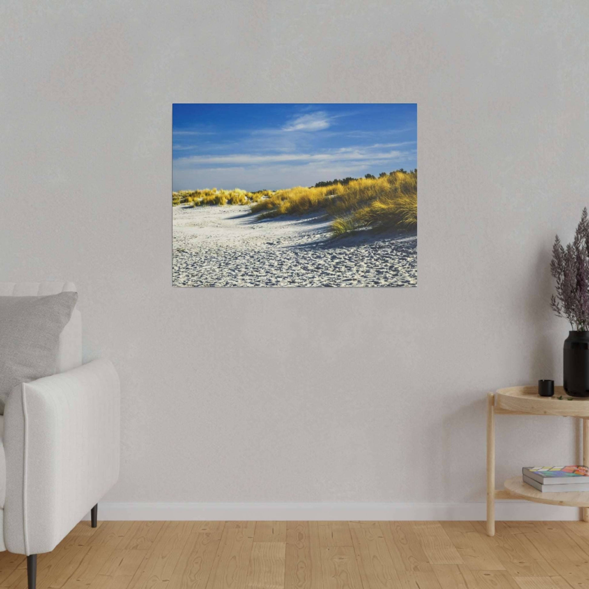 Photo of a sandy beach with golden dune grasses under a blue sky, hung on a light gray wall.
