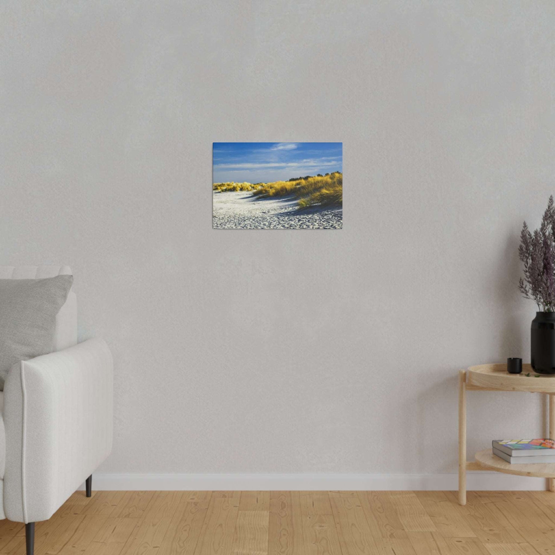 Small framed landscape photo of a sandy beach with golden dunes under a blue sky, hung on a light gray wall.
