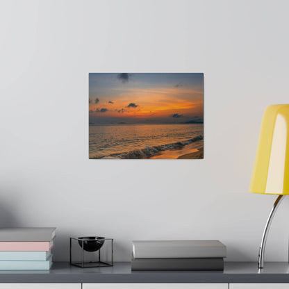 Framed photo of a sunset over the ocean with orange clouds and gentle waves, hung on a white wall above a shelf.