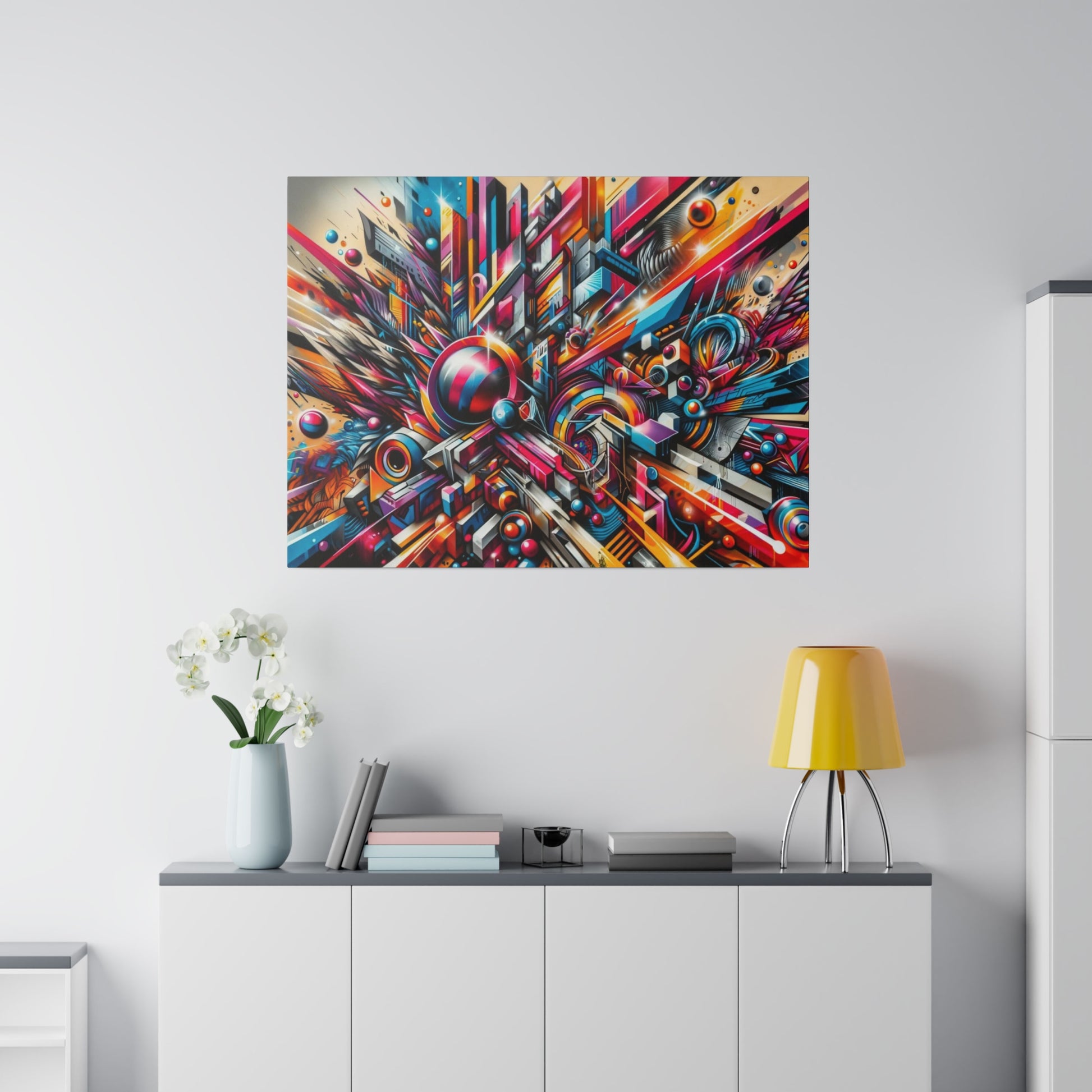 Colorful abstract geometric painting hung above a white sideboard with a pale vase, books, and a yellow lamp.