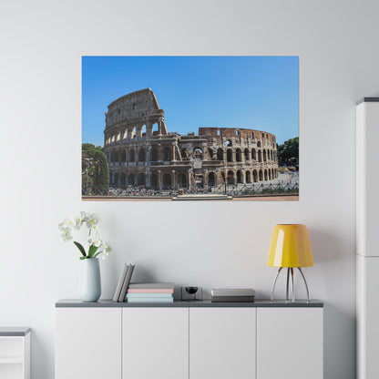 Photo of the Roman Colosseum in Rome, showing its stone arches and surrounding area against a clear blue sky.