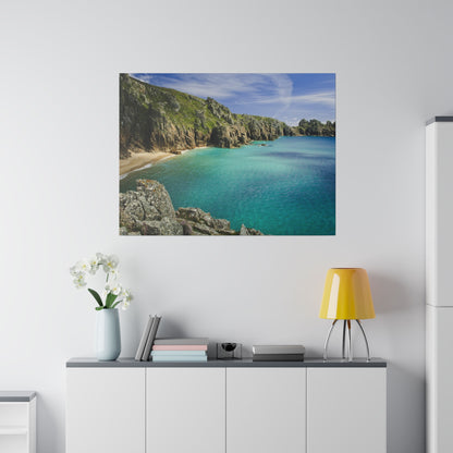 Framed wall art depicting a turquoise sea cove with rocky cliffs and a sandy beach above a white cabinet in a minimalist room.