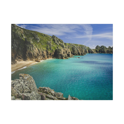 Turquoise sea surrounds a sandy cove bordered by rugged gray rock cliffs and green hills.