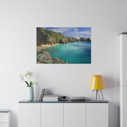 Framed coastal landscape with turquoise water, rocky cliffs, and a sandy bay on a white wall above a cabinet.