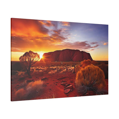 Desert scene with Uluru rock at sunset, orange sky, and sparse desert vegetation in the foreground.