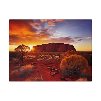 Desert landscape canvas print of Uluru at sunset, with orange-red sky, sparse shrubs, and rocky foreground.