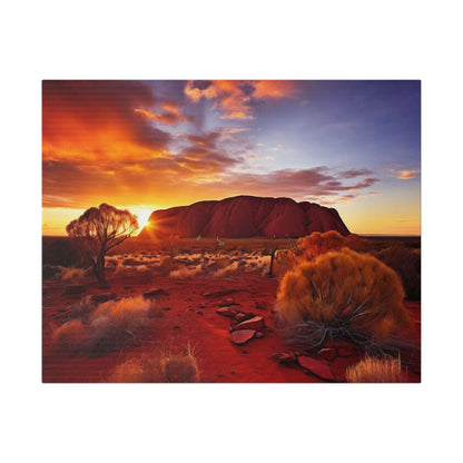 Desert landscape with Uluru at sunset, orange sky, red sand, and sparse shrubs in the foreground.