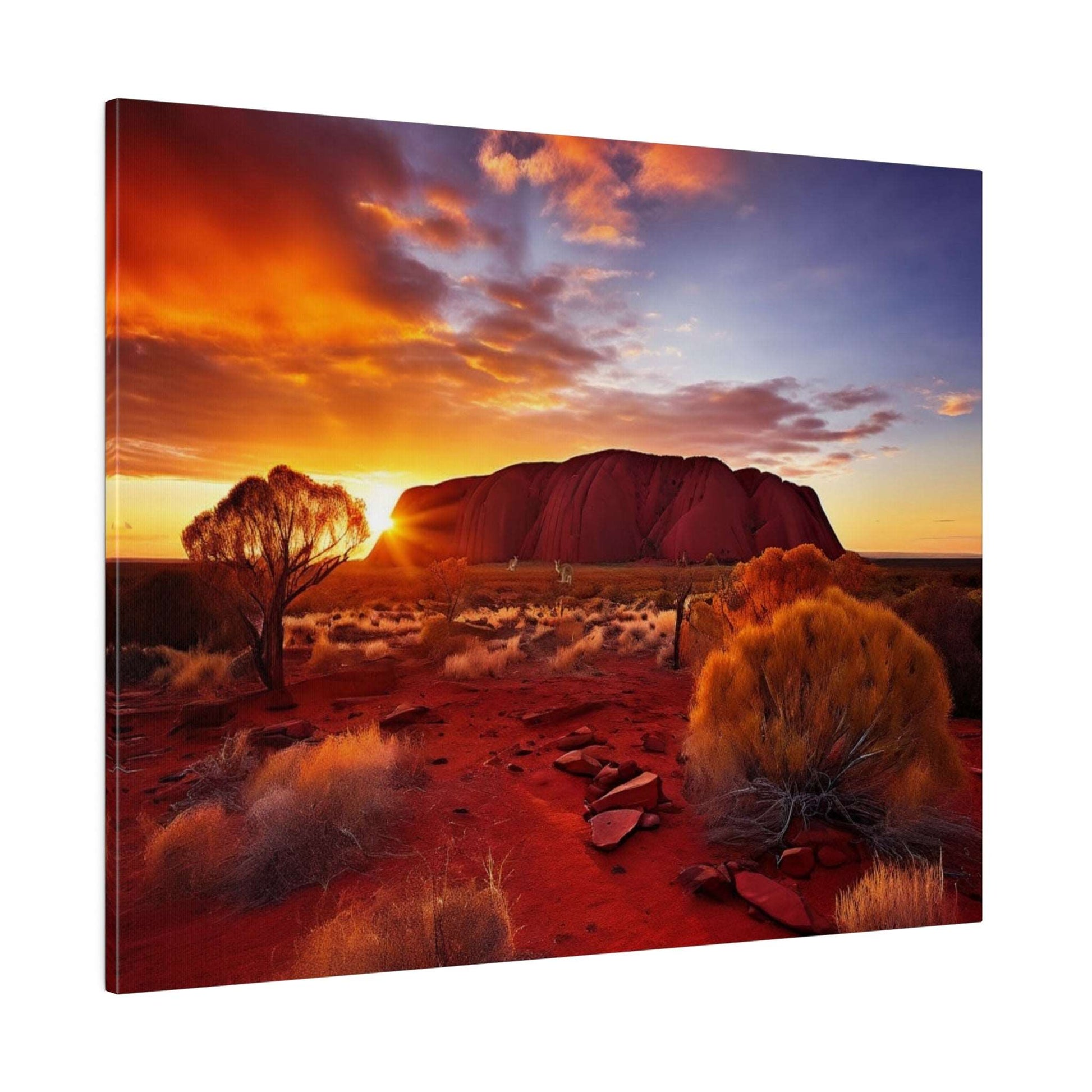 Canvas print showing Uluru at sunset with an orange-purple sky, red desert terrain, sun peeking behind the rock, and scattered bushes.