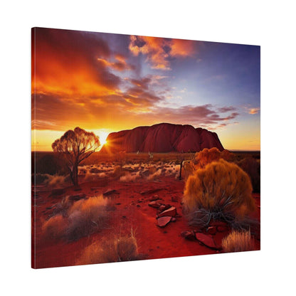 Desert landscape at sunset featuring Uluru in the distance, orange and purple sky, red soil, and sparse bushes.