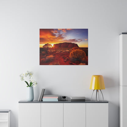 Desert landscape photo of Uluru at sunset hung on a white wall above a sideboard with a yellow lamp and vase.