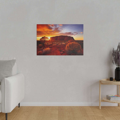 Desert sunset canvas print depicting Uluru with orange sky, red sand, and sparse shrubs.