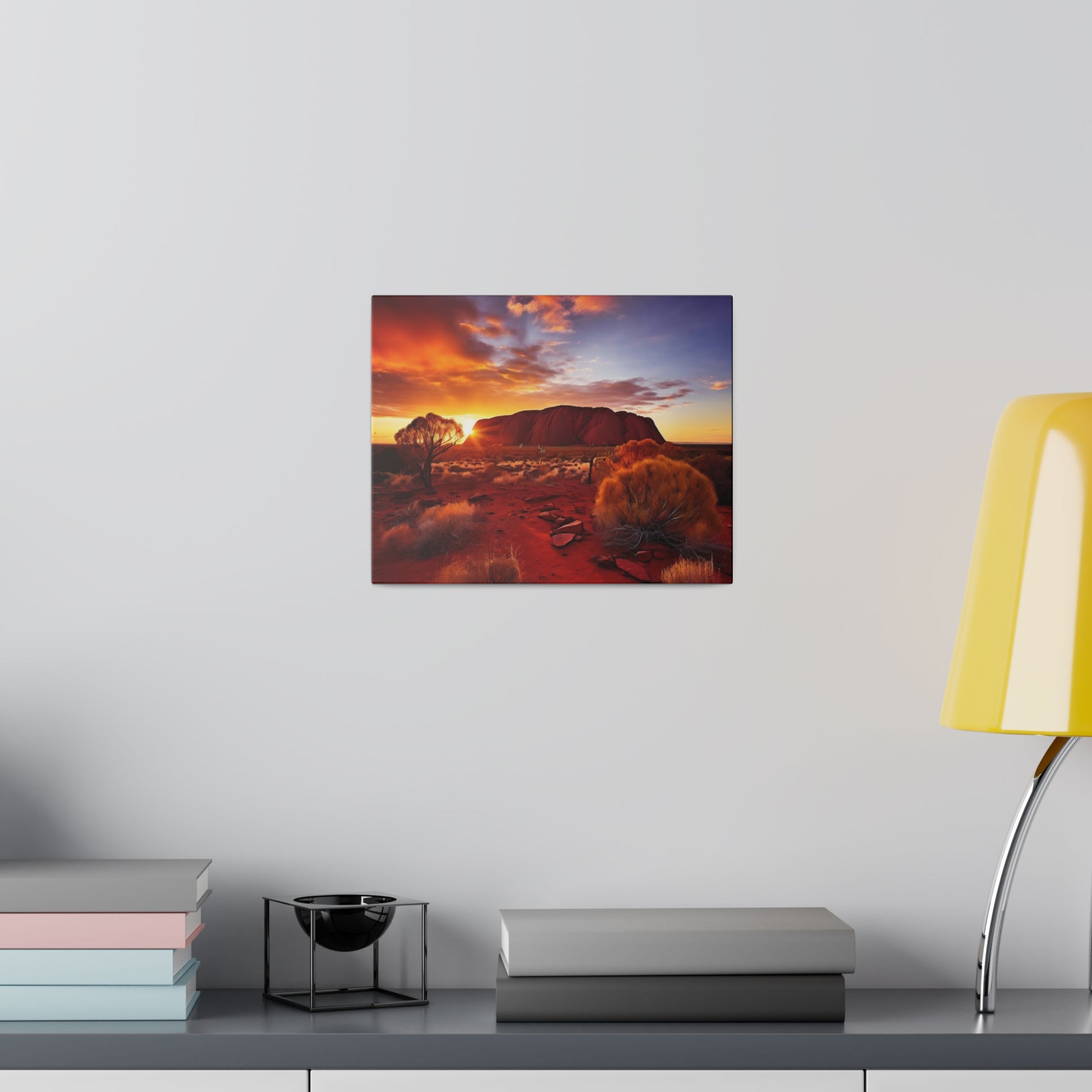 Canvas print of a desert sunset with red soil and shrubs, mounted on a light gray wall above a