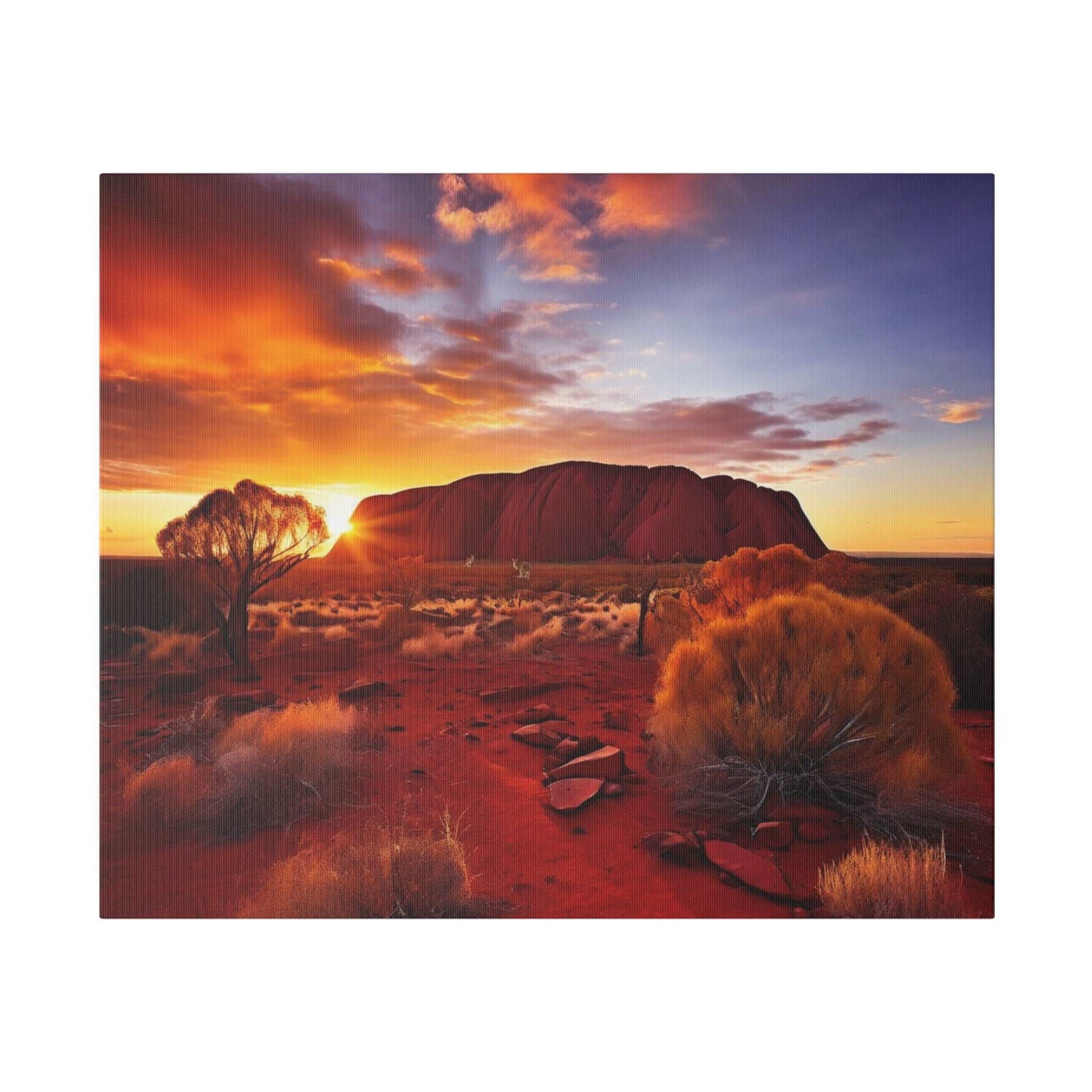 Desert landscape at sunset featuring Uluru, orange-red sand, sparse shrubs, and a lone tree on the left.