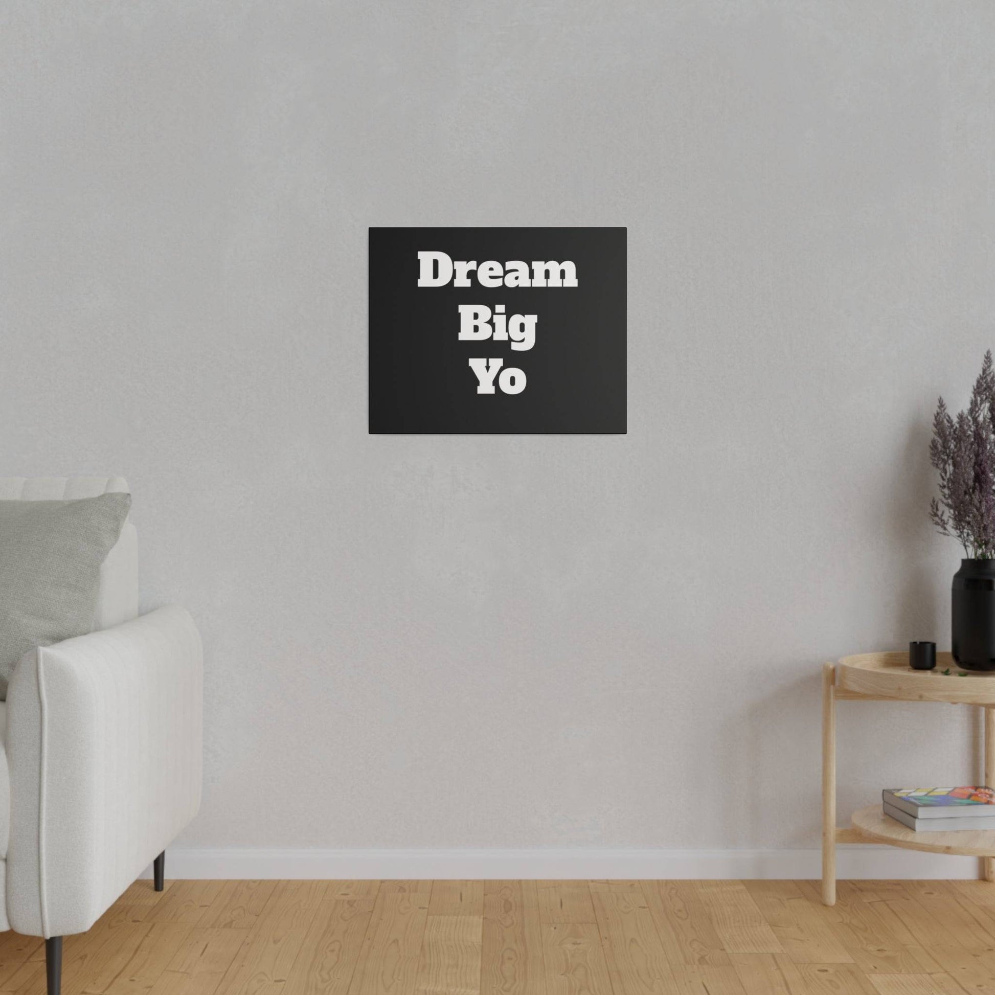 Black square wall art with bold white text "Dream Big Yo" hangs on a light gray wall in a living room.