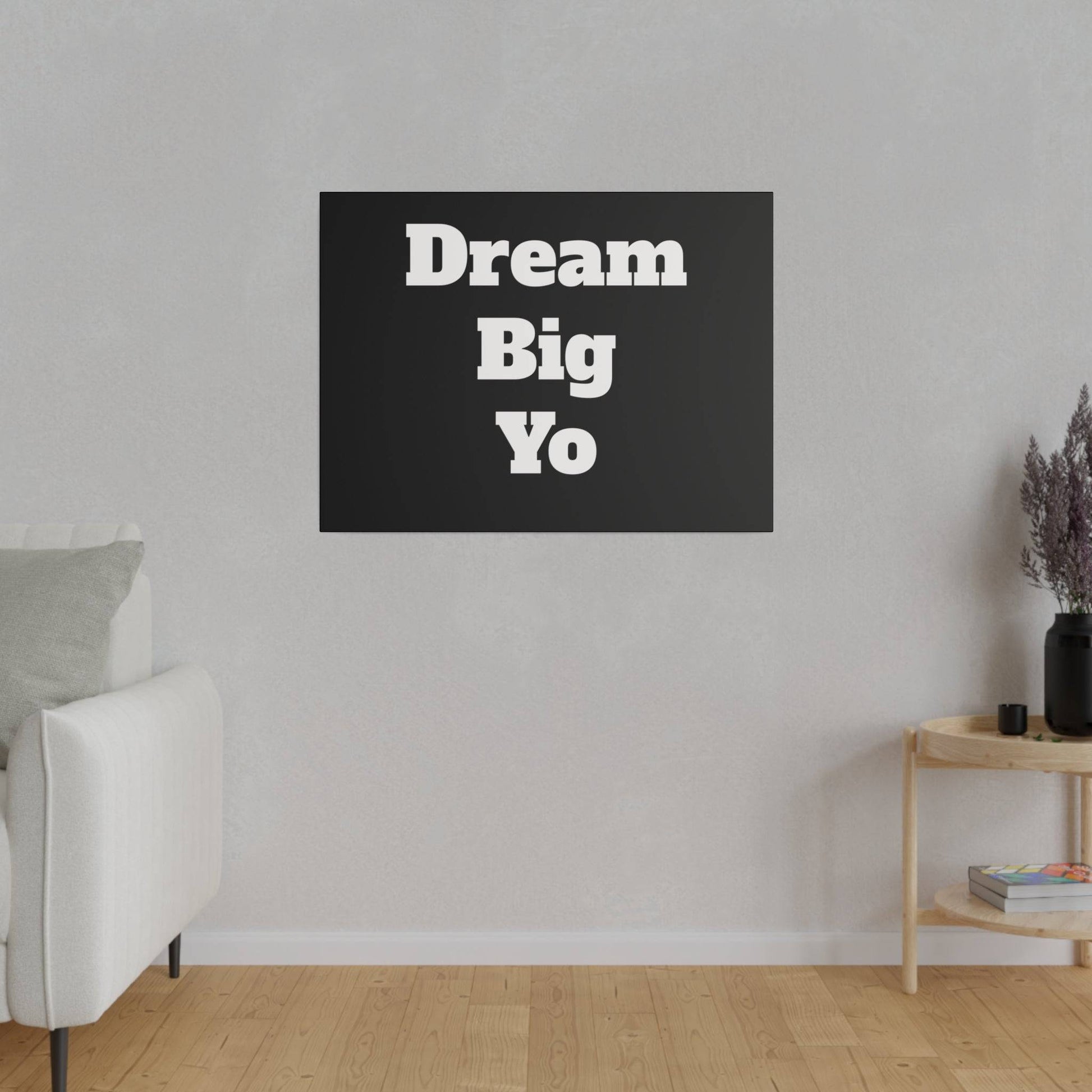 Black rectangular wall art with white bold text “Dream Big Yo” hanging on a light gray living room wall.