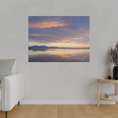 Framed landscape photo of a calm lake at sunset with distant mountains and an orange-purple sky reflected on water.