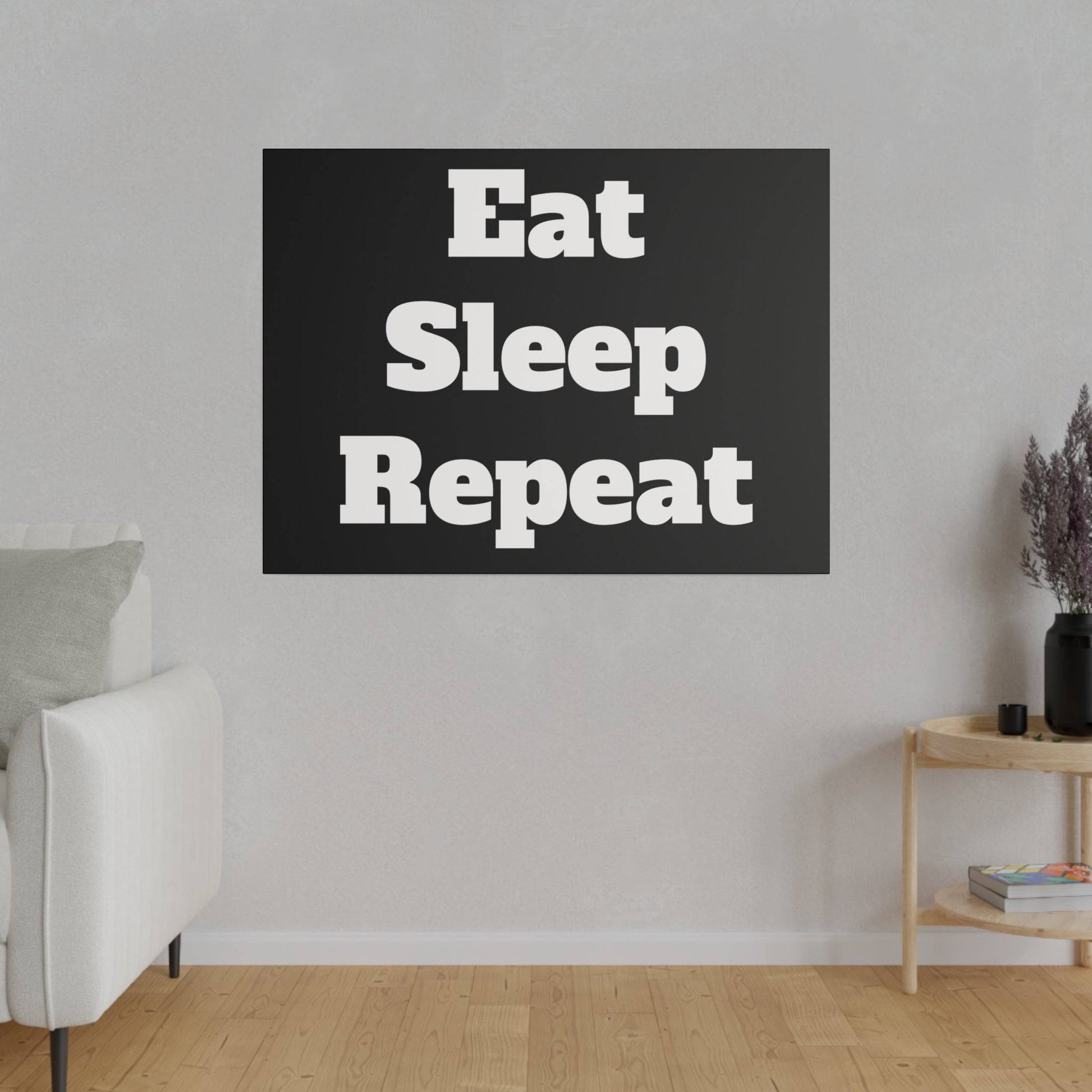 Black wall art with bold white text “Eat Sleep Repeat” hanging above a light sofa in a minimalist living room.