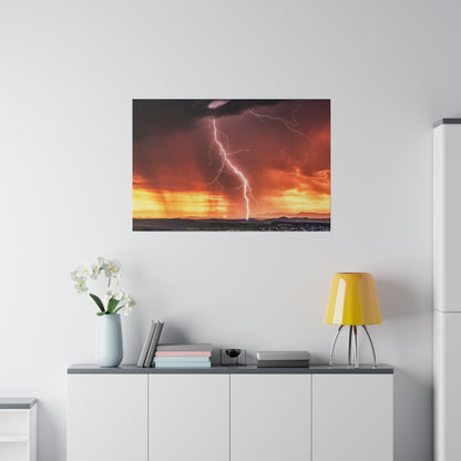 Wall art print of a thunderstorm with a bright lightning bolt over an orange-yellow sunset sky above a distant horizon.