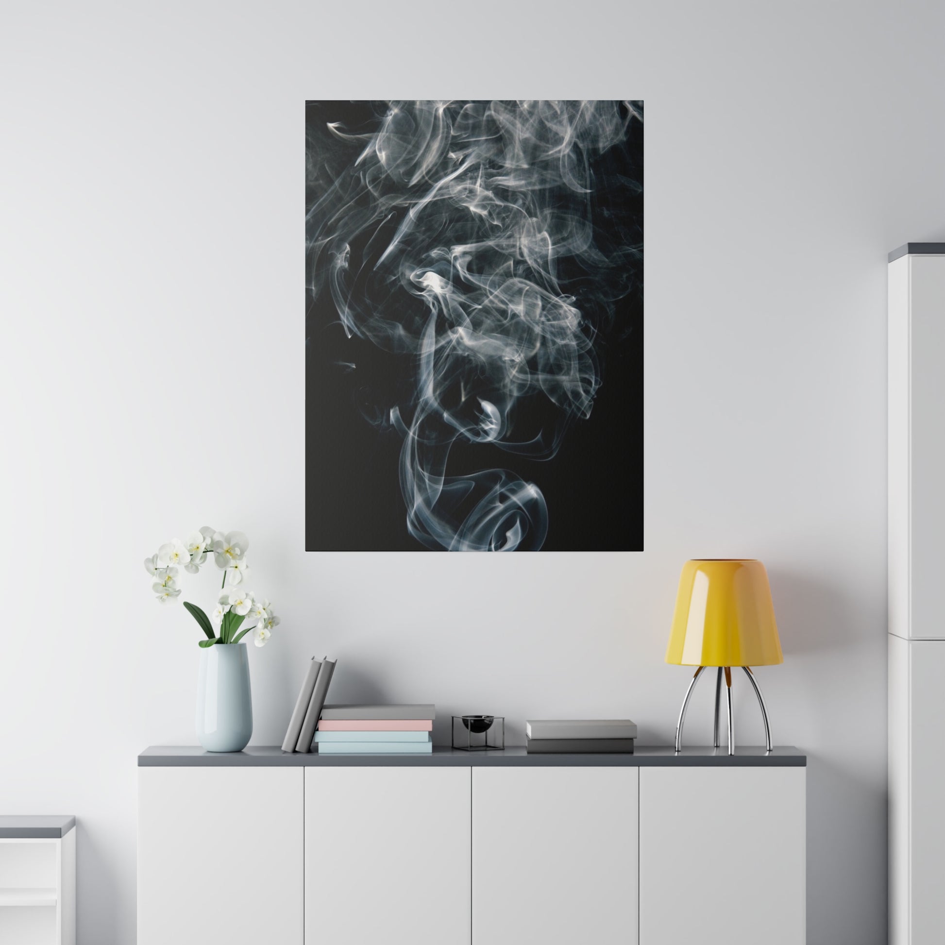 Vertical canvas print of white smoke swirls on a black background, mounted above a white cabinet with a yellow lamp.