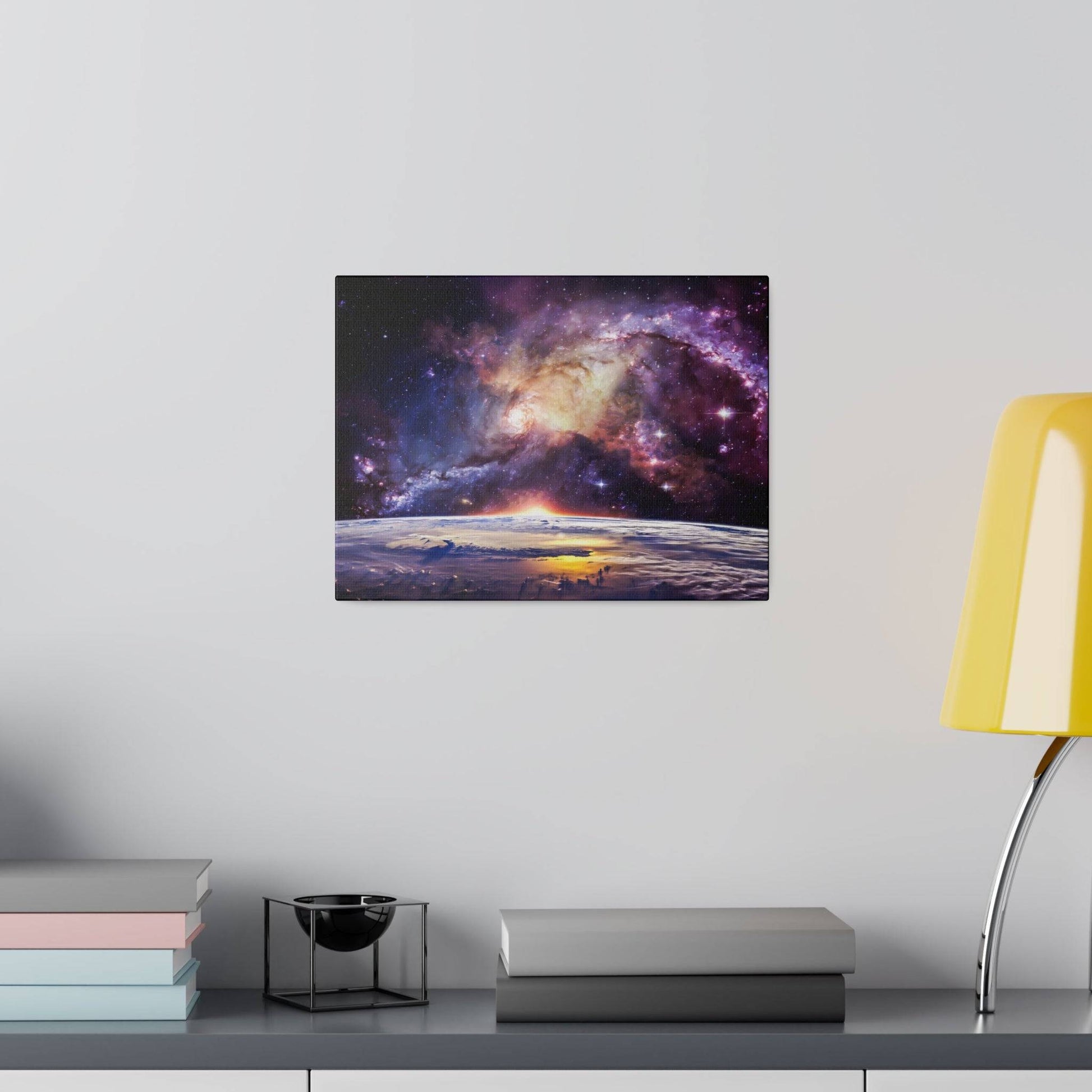 Space galaxy canvas print mounted on a light gray wall, with a yellow lamp and stacked books on a shelf below.