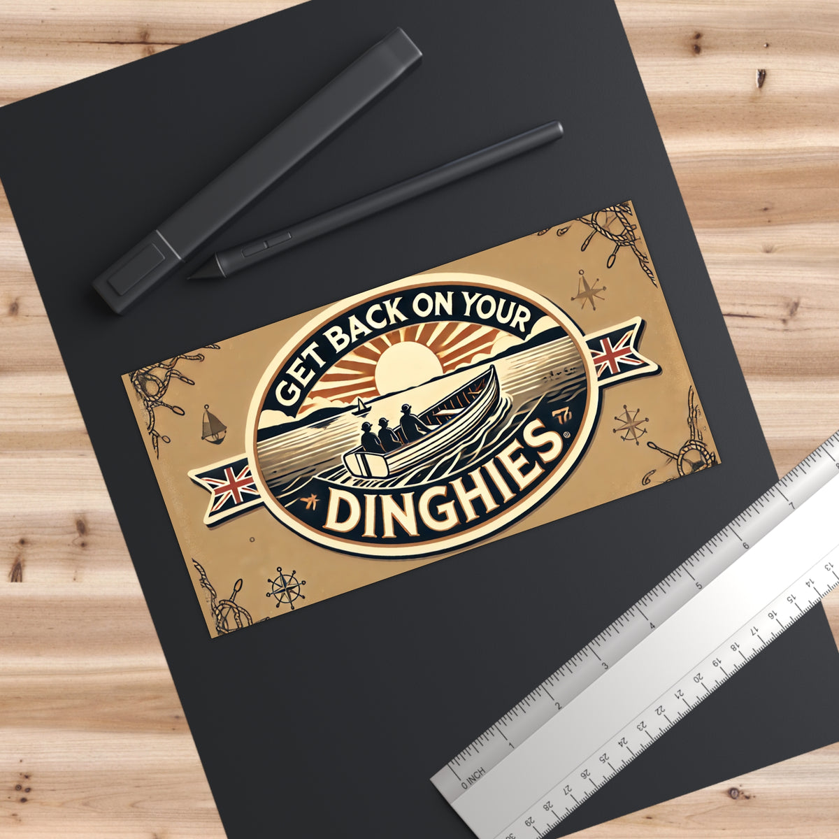 Beige poster with a boat and sun illustration and the text “Get Back On Your Dinghies,” on a dark mat beside a ruler and stylus.