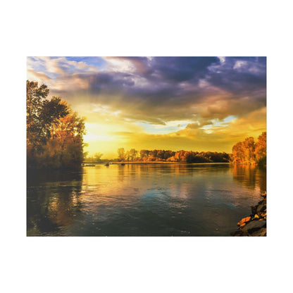 River at sunset with golden-orange light, calm water reflecting the colorful sky and tree-lined banks.