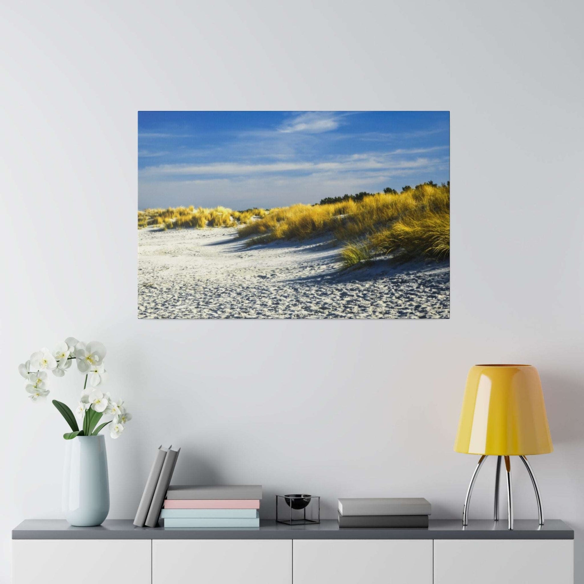 A photograph of a sandy beach with dunes and tall golden grasses under a blue sky.