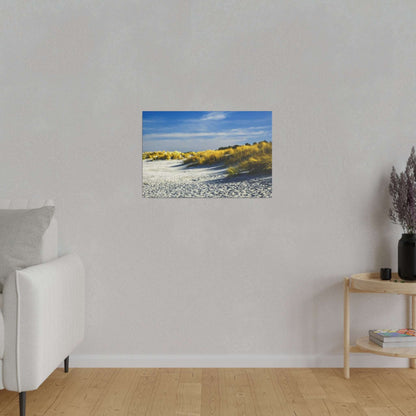 Small horizontal photograph of a beach with white sand dunes and golden grasses under a blue sky.