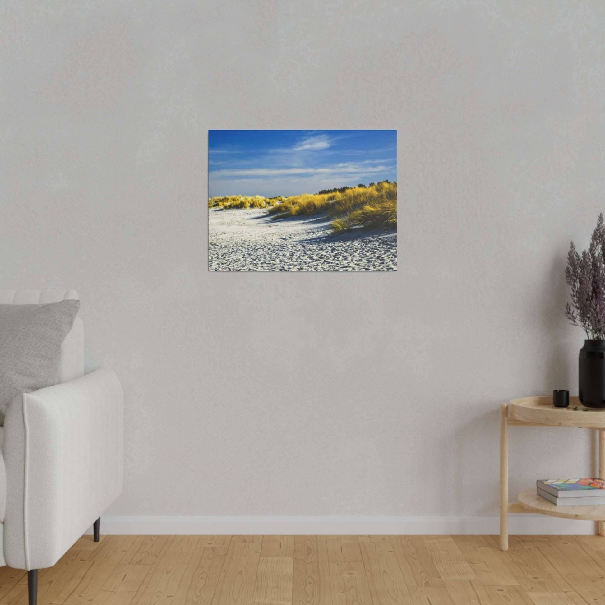 Framed coastal scene of white sand dunes with yellow grasses and a blue sky hangs on a light gray wall.