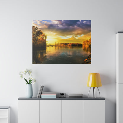 Framed landscape photograph of a sunset over a river with trees along the banks, hung above a white cabinet.