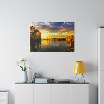 Framed sunset river landscape photograph on a white wall above a cabinet with a yellow lamp and white vase flowers.