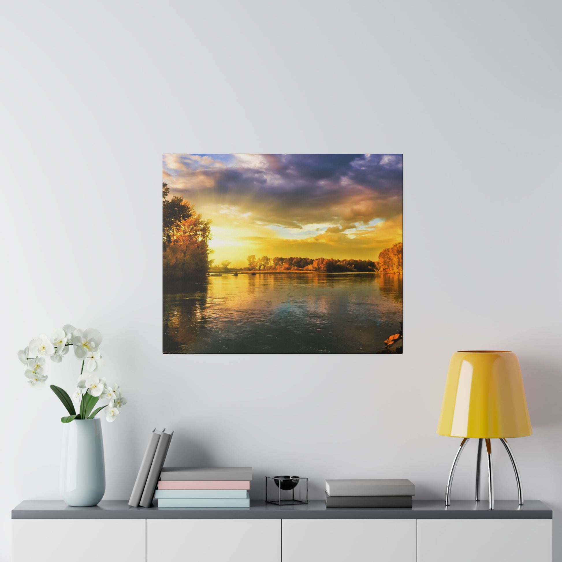 Square wall art showing a sunset over a calm river with golden light and trees along the banks.
