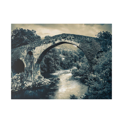 Monochrome canvas print showing an ancient stone arch bridge over a flowing river, with dense trees along the banks.