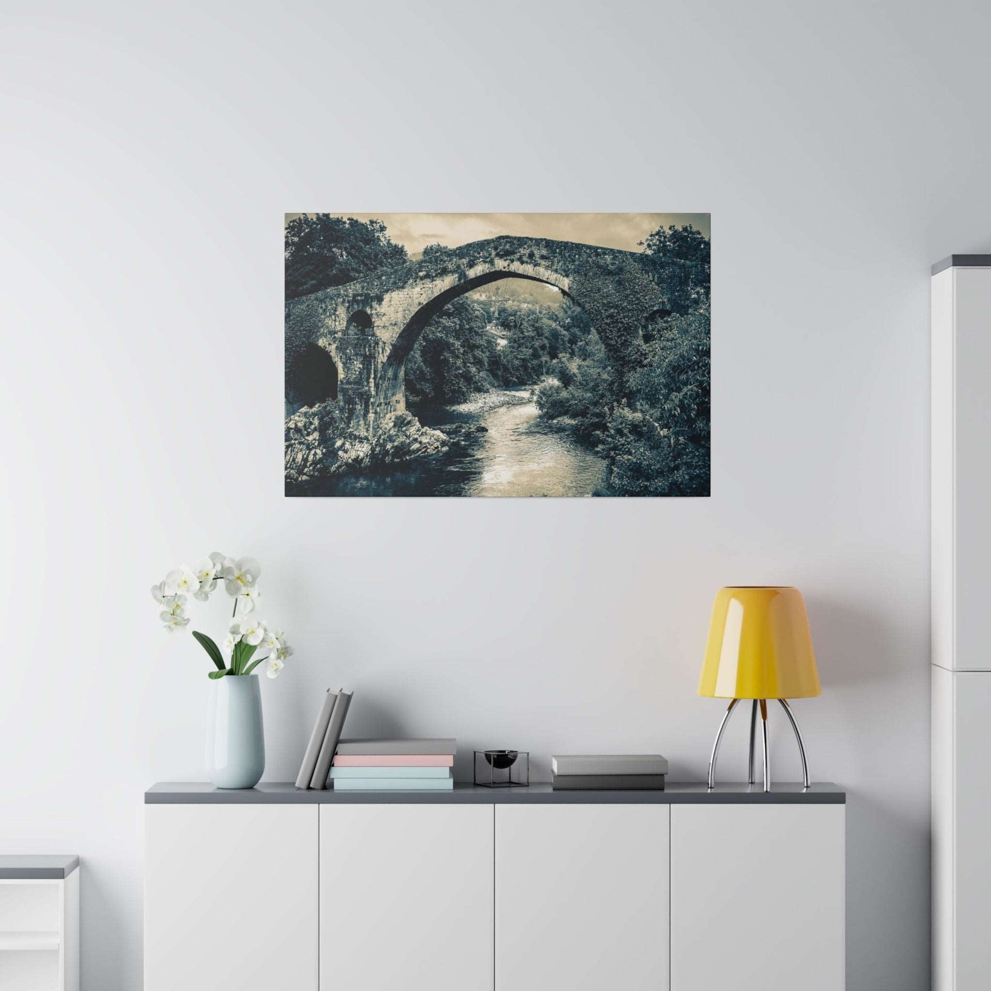 Monochrome canvas print of a historic stone arch bridge over a river, mounted on a light wall above a cabinet.