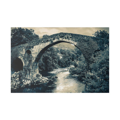 Monochrome blue-toned image of a historic stone arch bridge spanning a river, surrounded by dense trees and rocky banks.