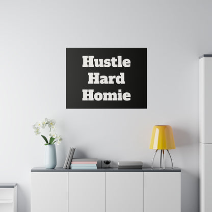 Black square poster with bold white text “Hustle Hard Homie” on a wall above a gray cabinet with books, vase, and a yellow lamp.