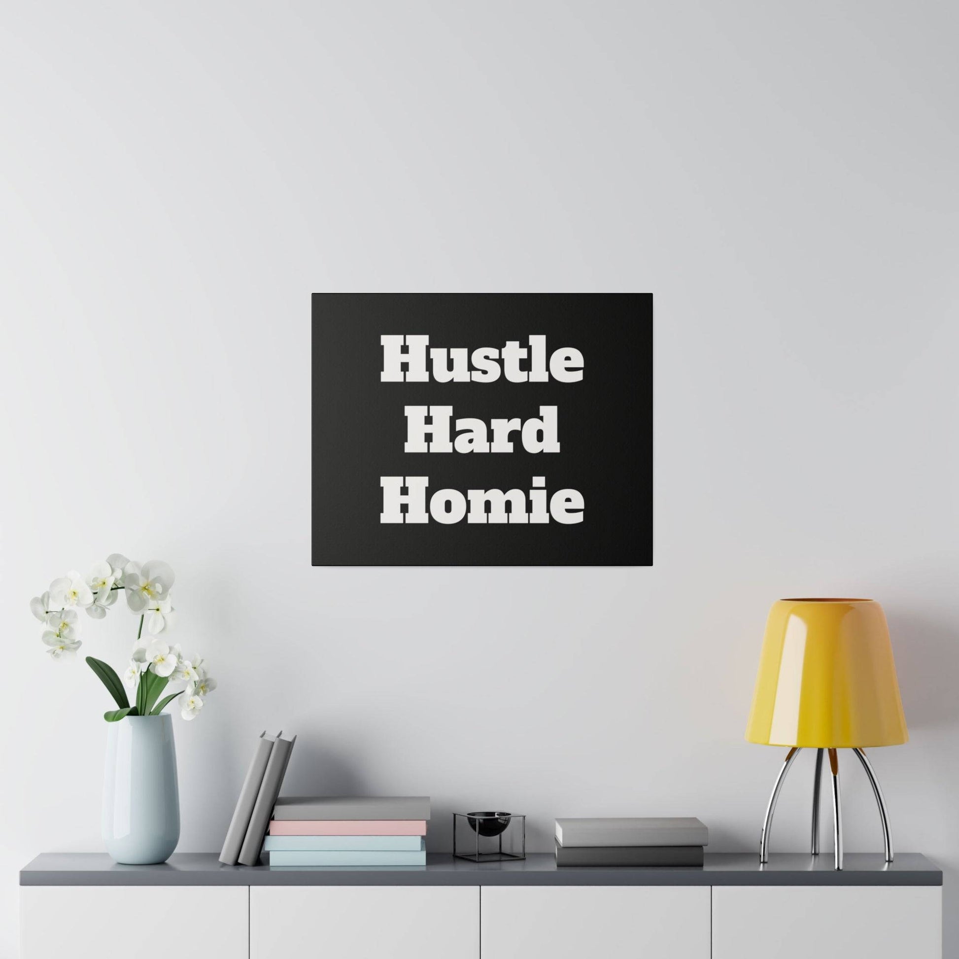 Black square wall art with bold white lettering reading “Hustle Hard Homie” mounted above a cabinet.