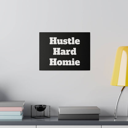 Black rectangular wall art with white bold text "Hustle Hard Homie" mounted over a shelf with pastel book stacks, a black decorative bowl,