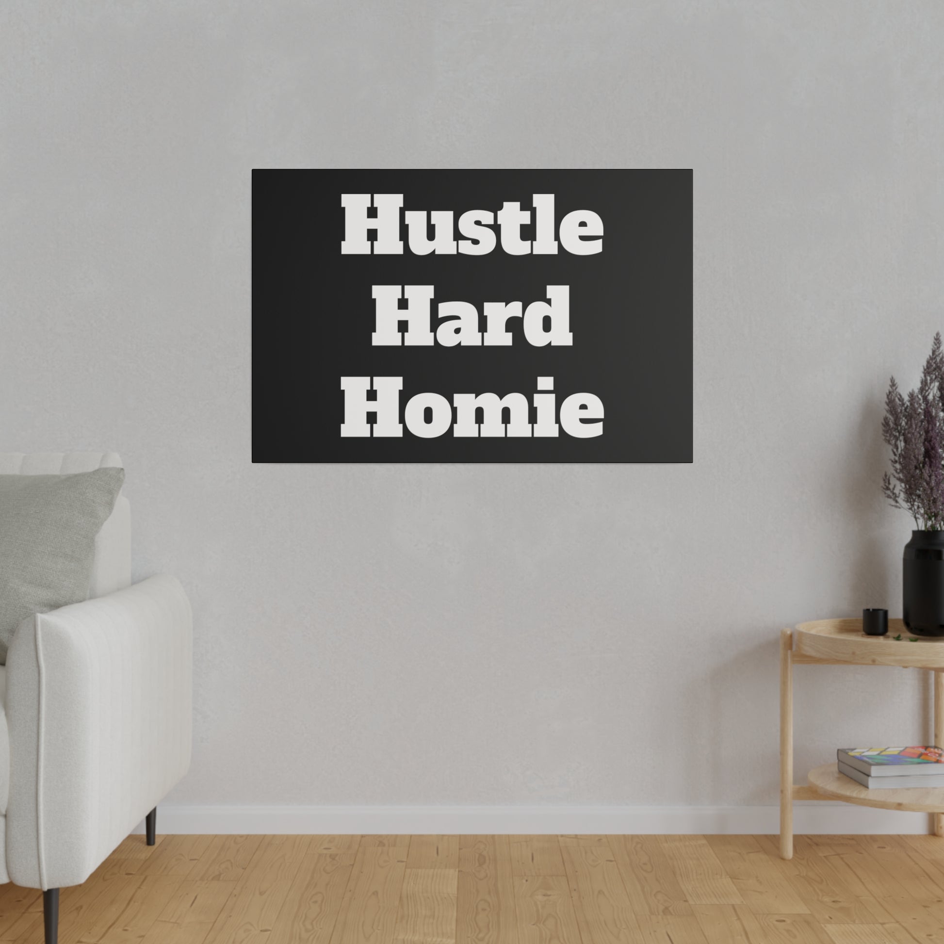 Living room wall with a black poster reading "Hustle Hard Homie" above a white sofa and a wooden side table.
