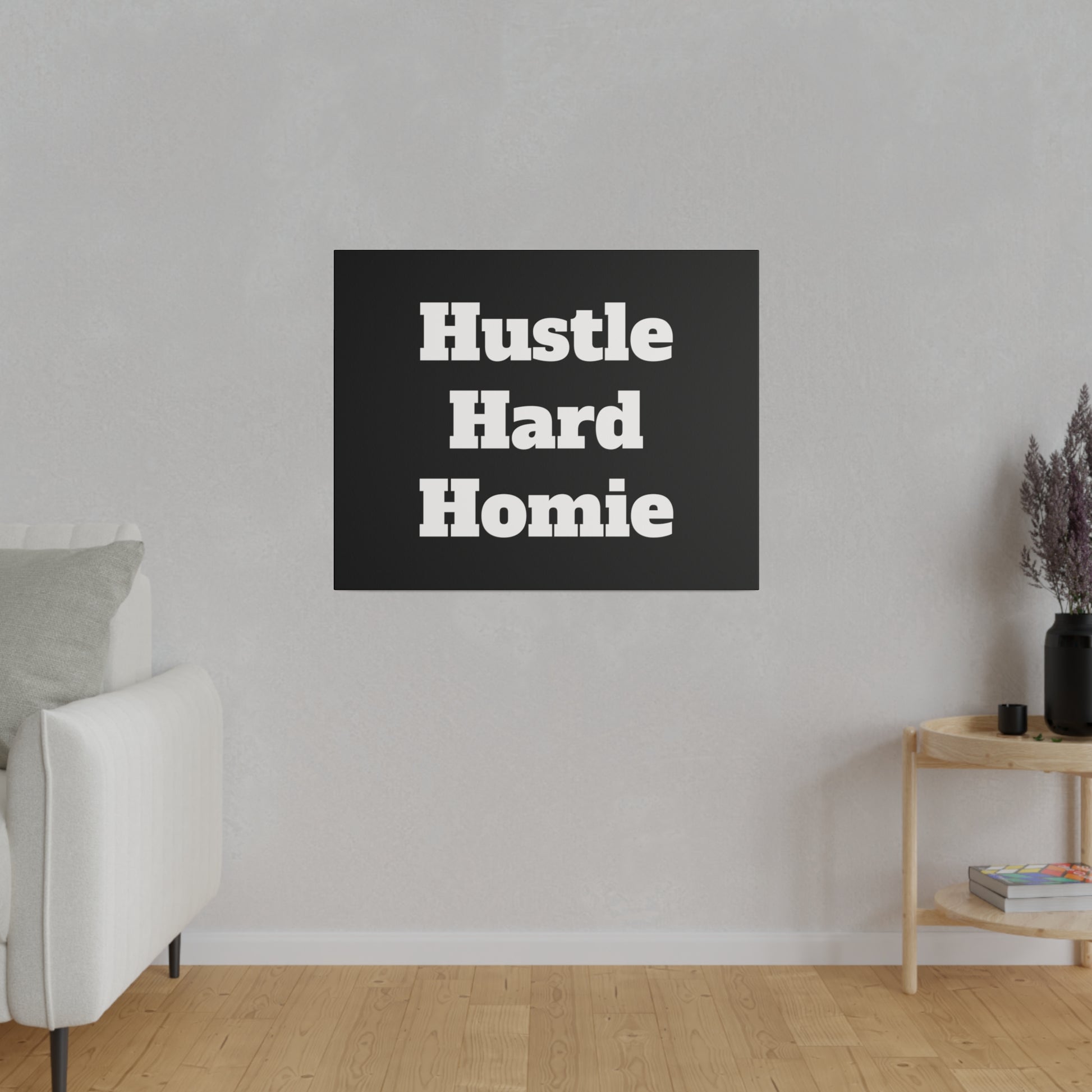 Living room wall features a black square sign reading Hustle Hard Homie; a beige sofa on the left and a wooden side table on the right.