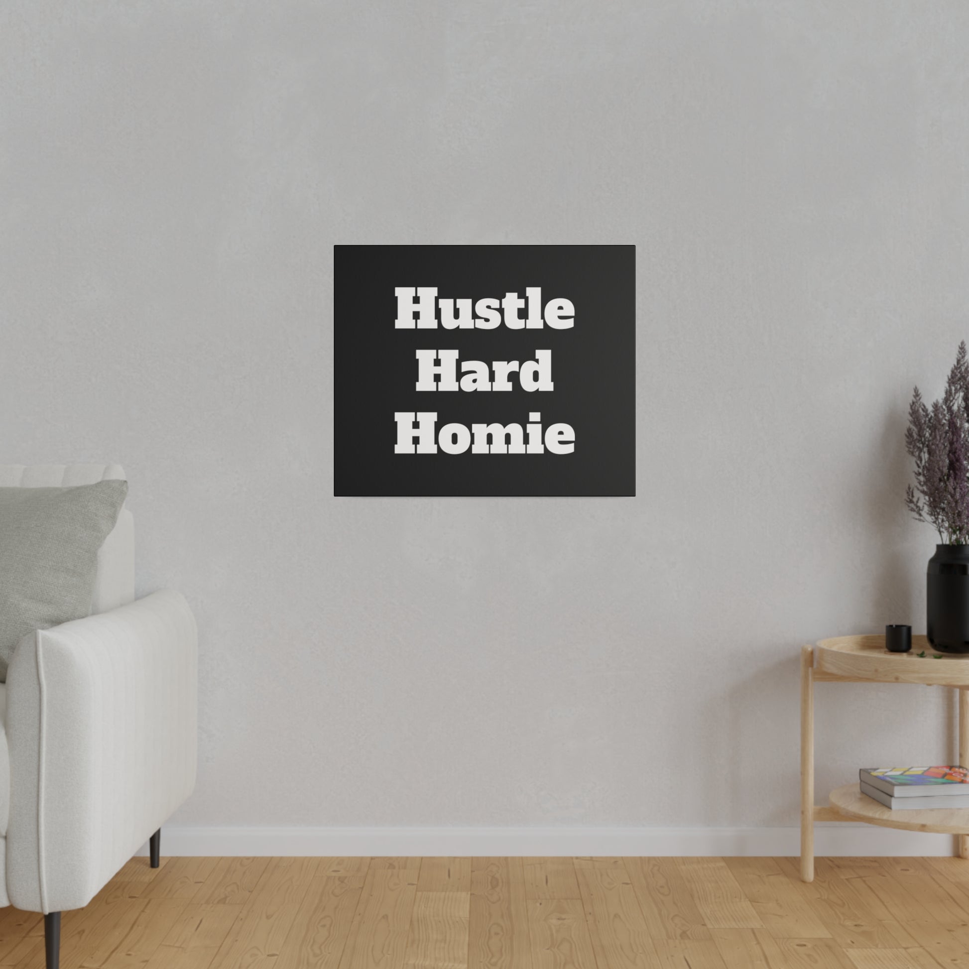 Living room wall with a black square poster reading "Hustle Hard Homie" above a white sofa and wooden side table.