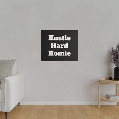 Living room wall with a black square poster reading "Hustle Hard Homie" above a white sofa and wooden side table.