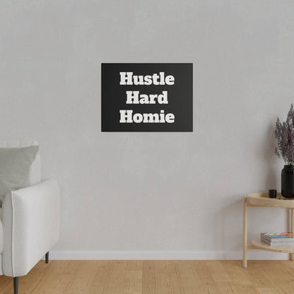 Small black wall art with white bold text “Hustle Hard Homie” mounted on a light gray wall above a wooden side table.